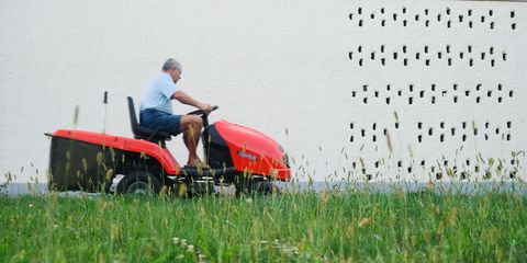 Hausmeister mäht mit einer Mähmaschine den Rasen.