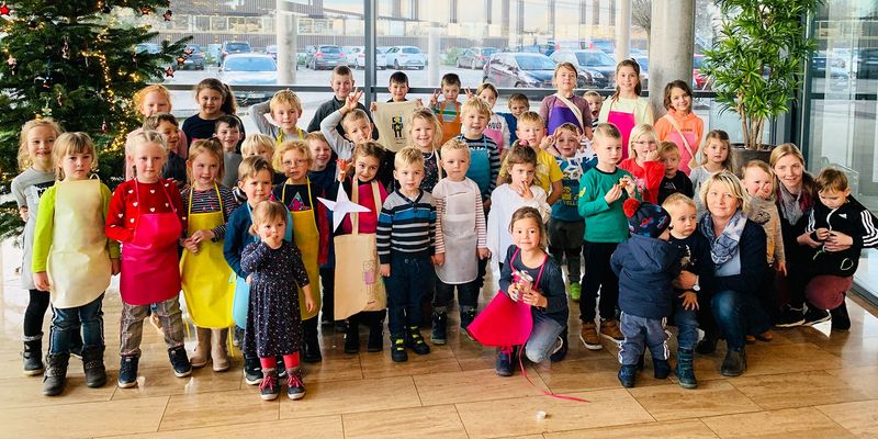 Gruppenfoto von Kindern und Erziehern vor einem Fenster mit Weihnachtsbäumen